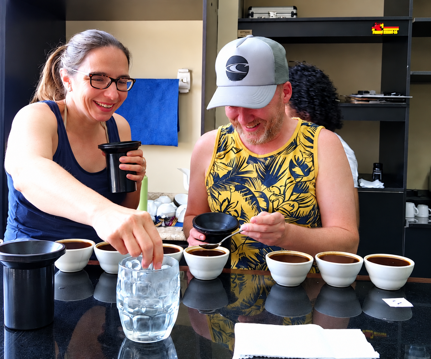 Dos viajeros comparten una cata de café entre sonrisas, con varias tazas sobre la mesa