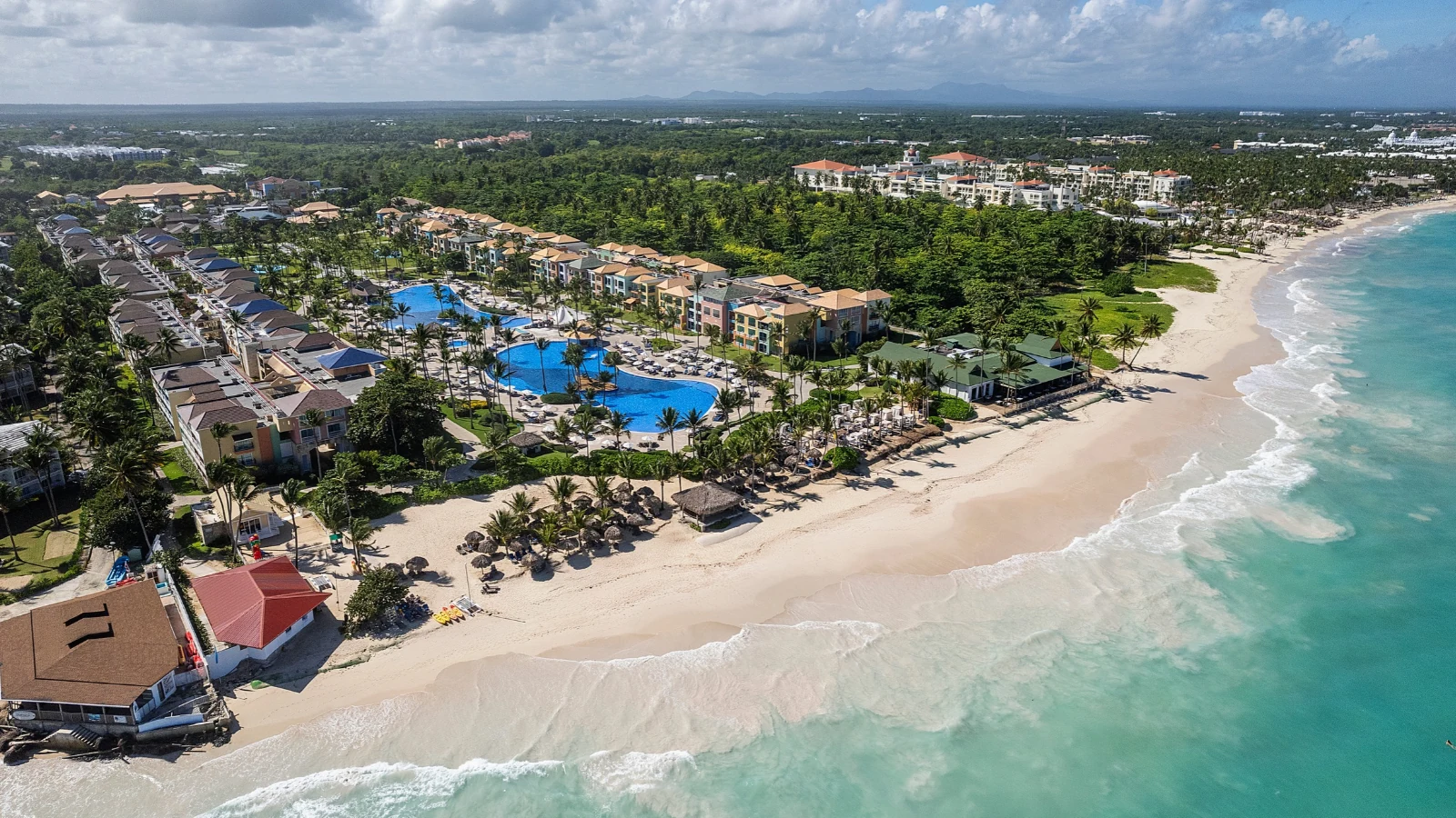 Vista aérea de un hotel junto a la playa, con piscinas y jardines